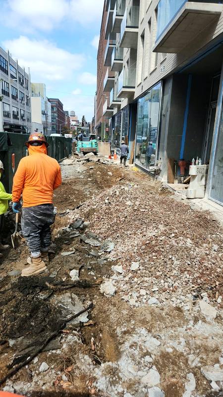 Crew excavating the old sidewalk down to subgrade beside a new mixed-use building — Platinum Concrete NY